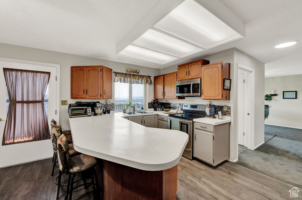 Kitchen with kitchen peninsula, appliances with stainless steel finishes, light hardwood / wood-style floors, and sink
