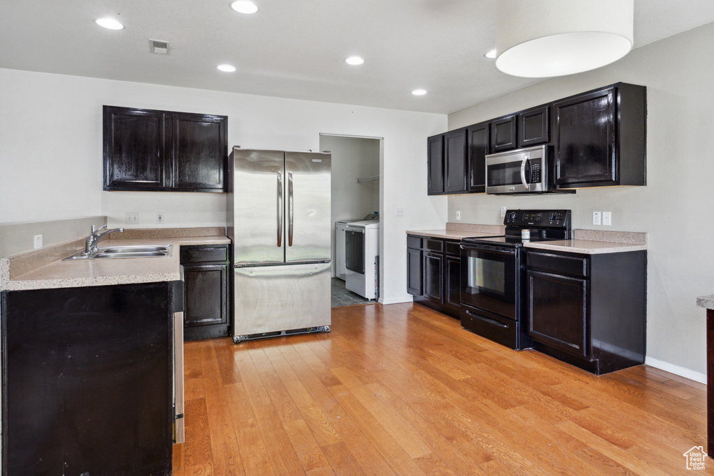 Kitchen featuring washer and clothes dryer, appliances with stainless steel finishes, sink, and light wood-type flooring