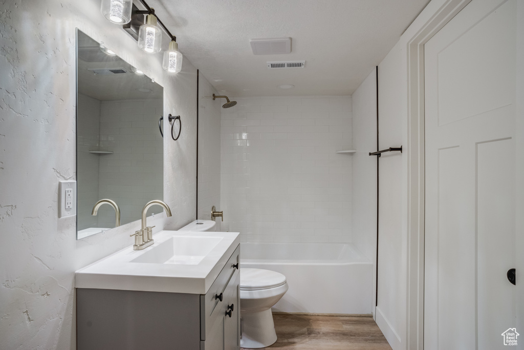 Full bathroom featuring toilet, oversized vanity, tiled shower / bath combo, and hardwood / wood-style floors