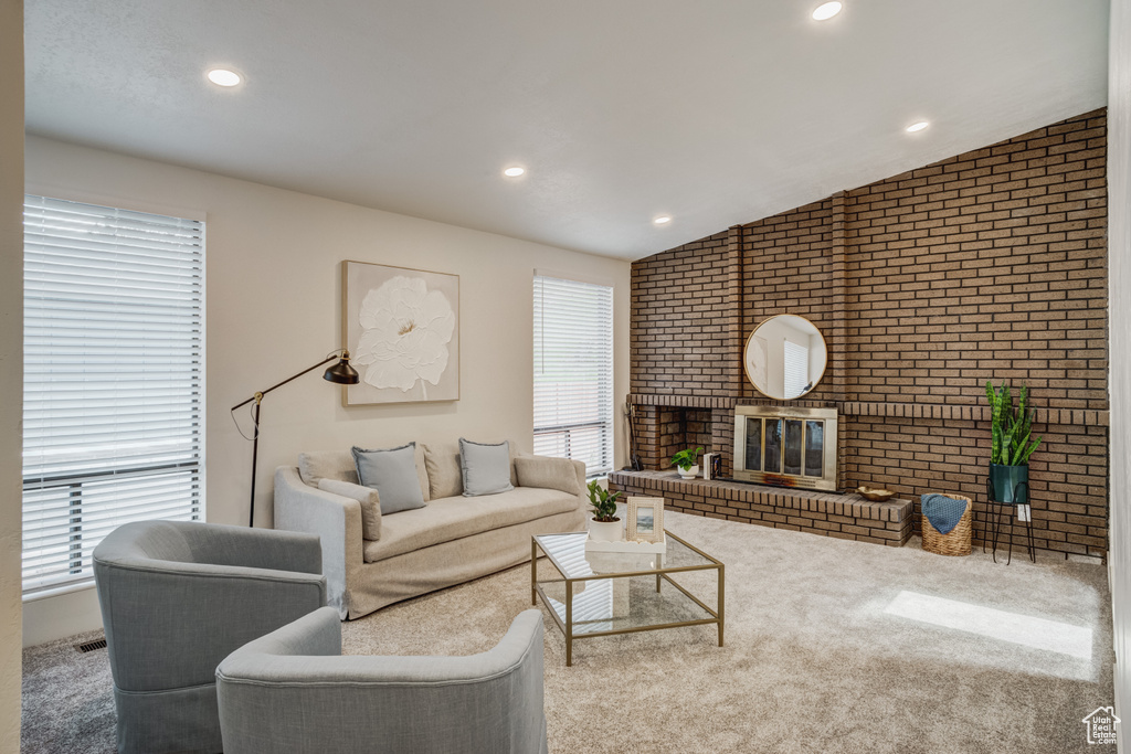 Carpeted living room featuring brick wall, vaulted ceiling, and a fireplace