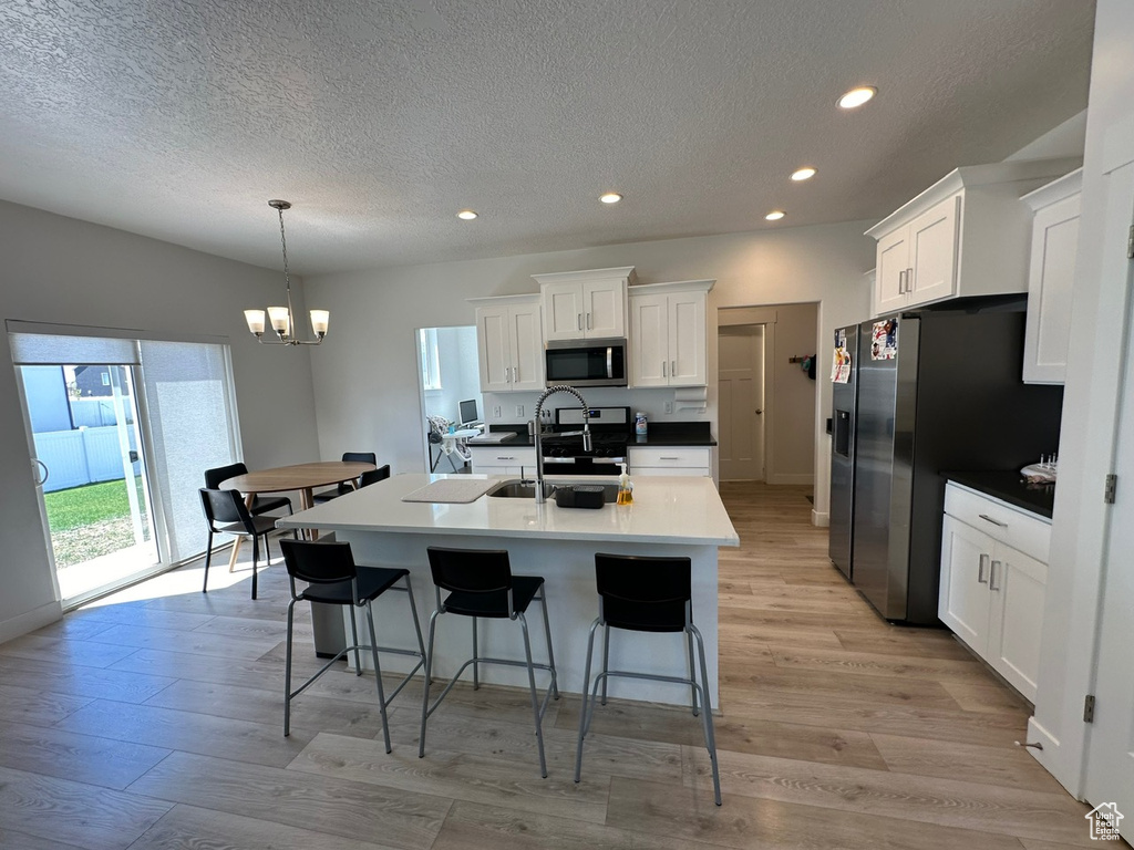 Kitchen featuring appliances with stainless steel finishes, light hardwood / wood-style flooring, hanging light fixtures, white cabinetry, and an inviting chandelier