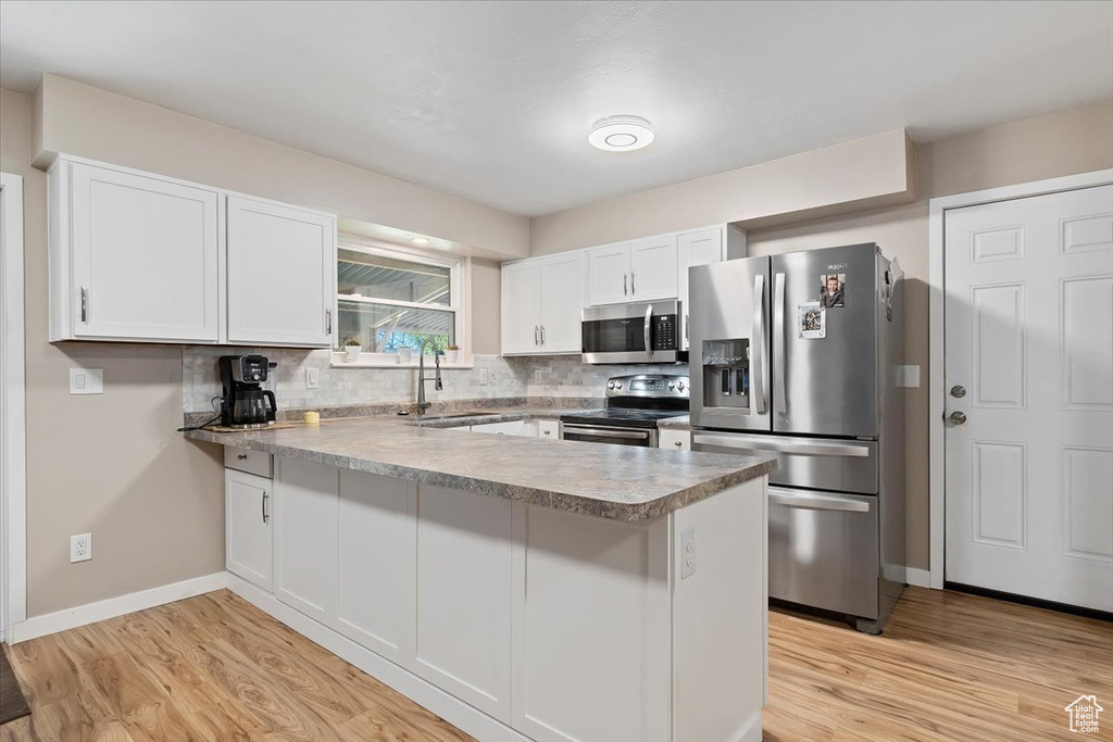 Kitchen with light wood-type flooring, white cabinetry, stainless steel appliances, sink, and tasteful backsplash