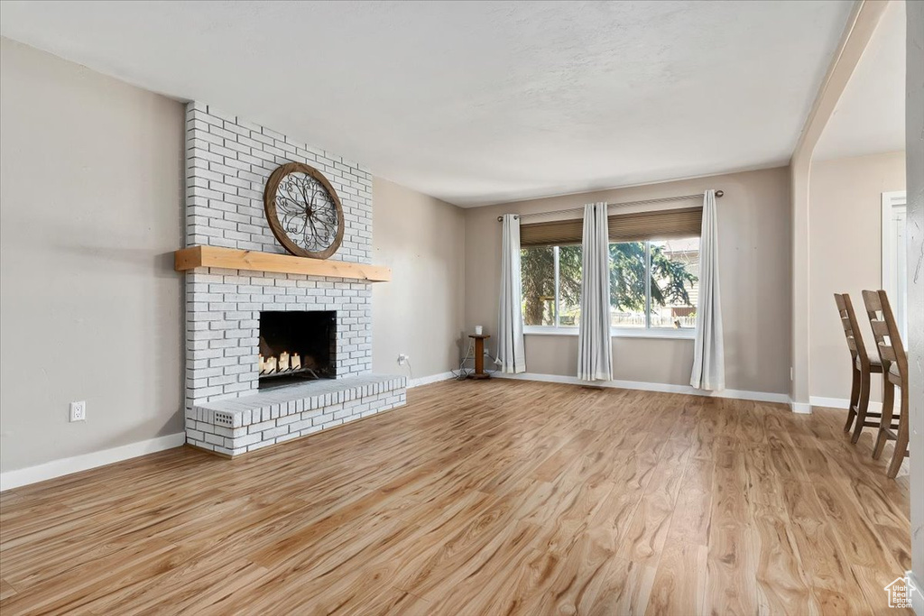 Unfurnished living room featuring light hardwood / wood-style floors, brick wall, and a brick fireplace