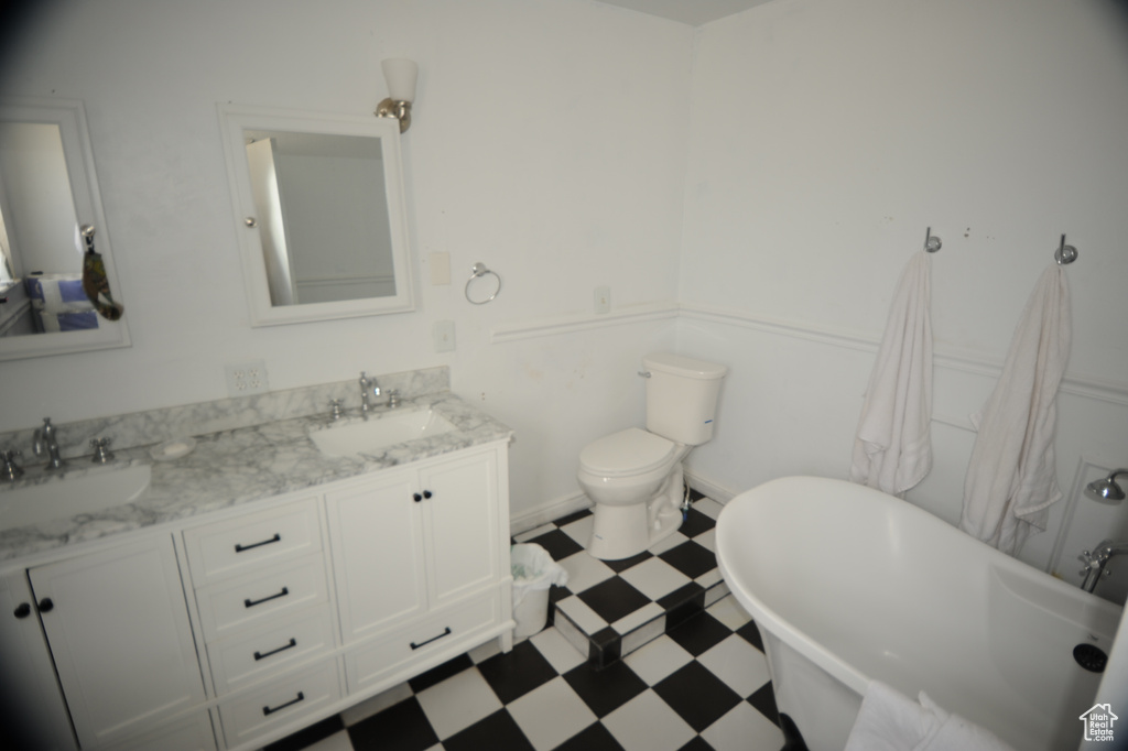 Bathroom featuring toilet, a bathing tub, vanity with extensive cabinet space, tile floors, and dual sinks