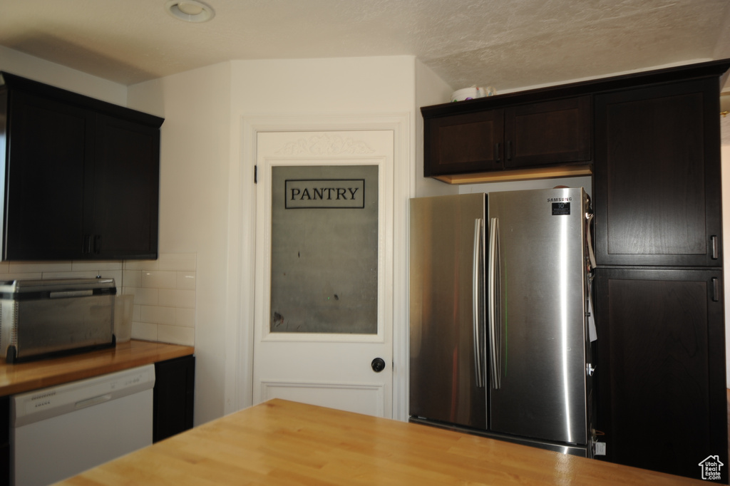 Kitchen with backsplash, wood counters, white dishwasher, and stainless steel fridge