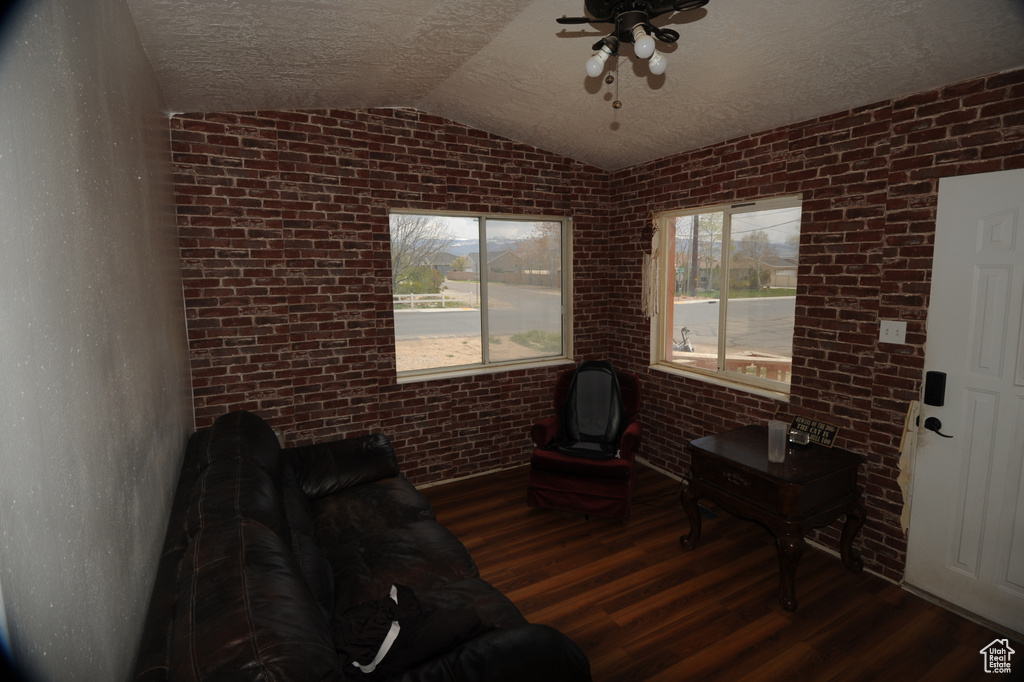 Unfurnished living room featuring dark hardwood / wood-style floors, lofted ceiling, ceiling fan, and brick wall