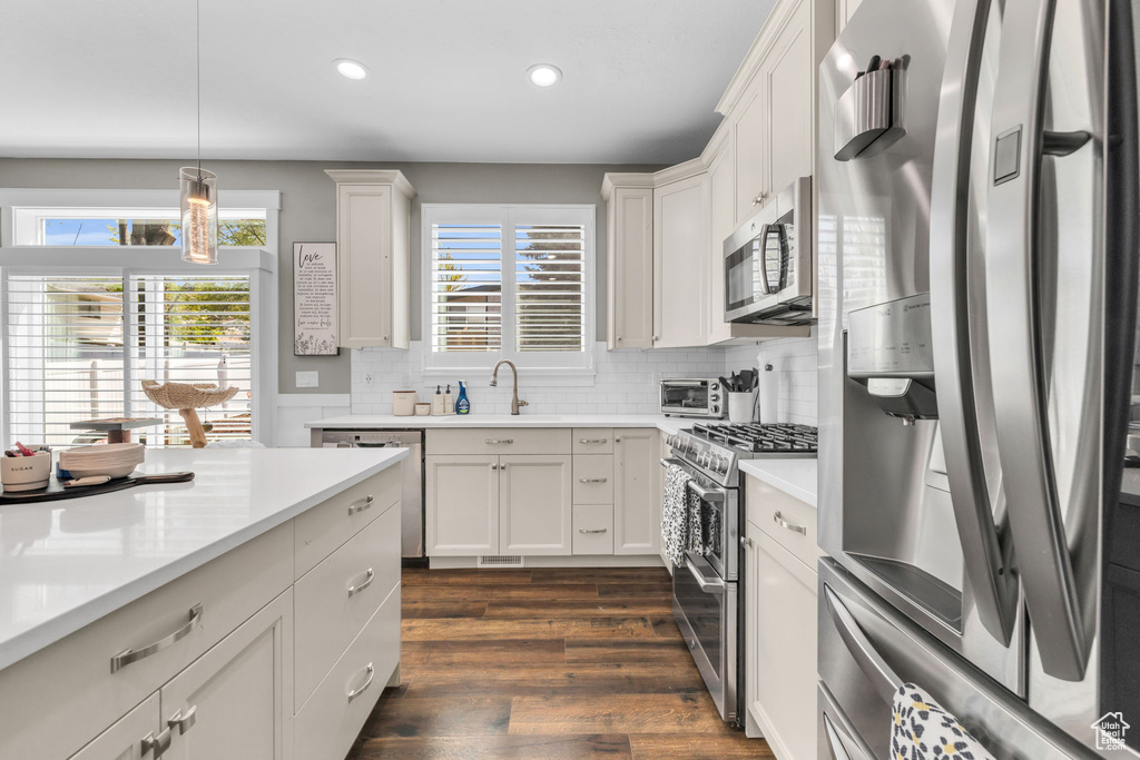 Kitchen featuring pendant lighting, dark wood-type flooring, appliances with stainless steel finishes, sink, and tasteful backsplash