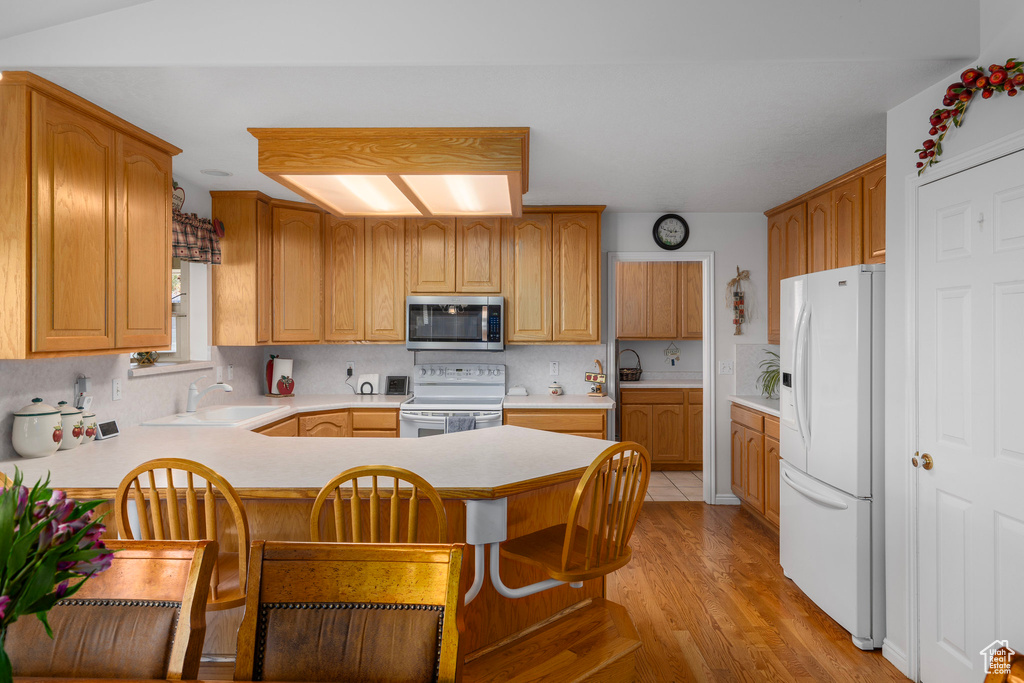 Kitchen with white appliances, kitchen peninsula, a kitchen bar, sink, and light hardwood / wood-style floors