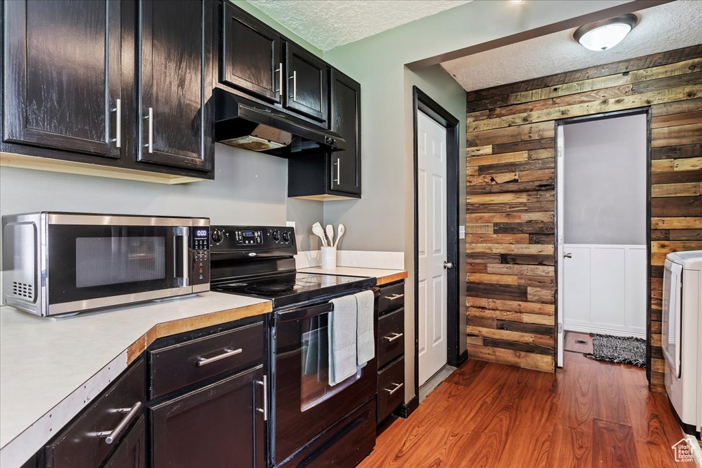 Kitchen with black electric range oven, washer / dryer, a textured ceiling, wooden walls, and hardwood / wood-style floors