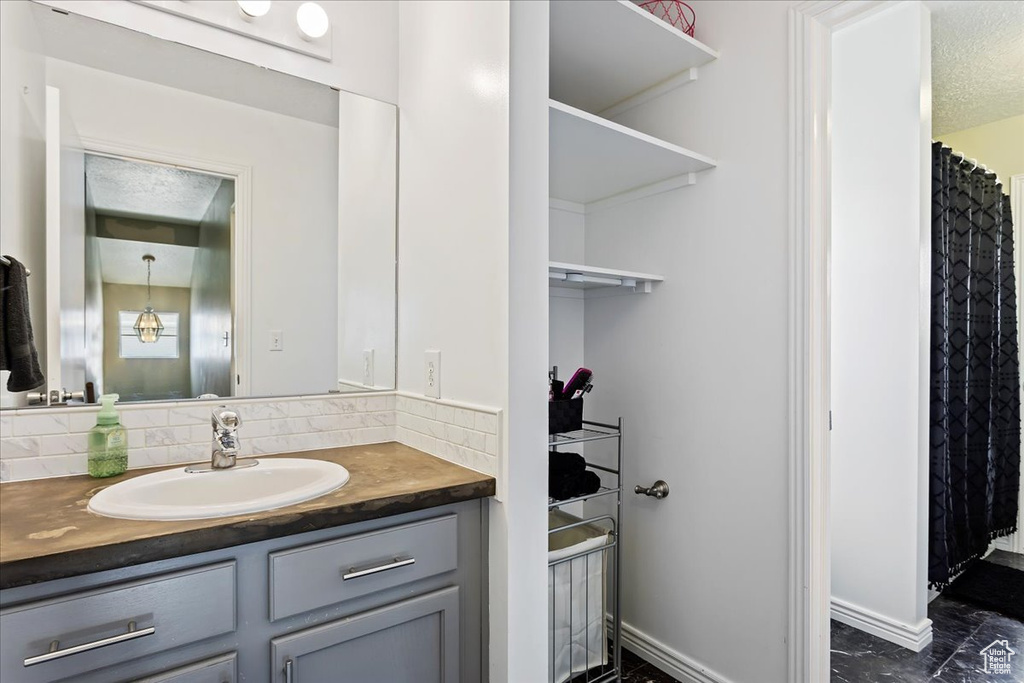 Bathroom featuring backsplash, a textured ceiling, tile floors, and vanity with extensive cabinet space