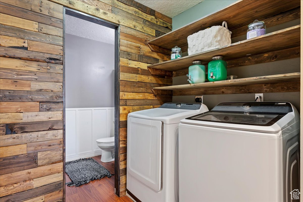 Laundry room featuring a textured ceiling, wood walls, hardwood / wood-style flooring, and washer and dryer