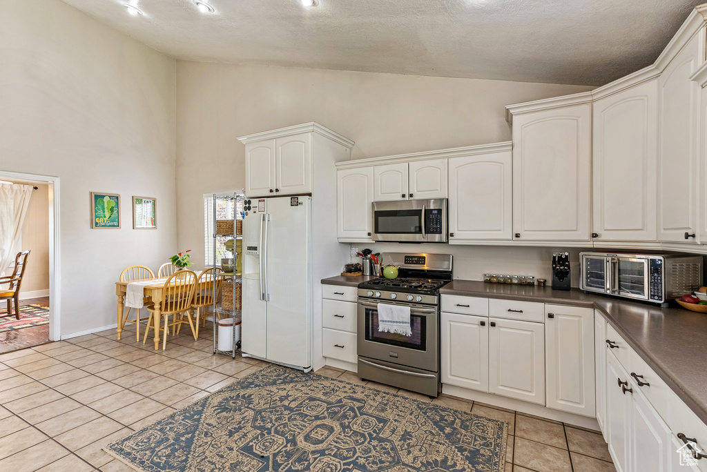 Kitchen with high vaulted ceiling, appliances with stainless steel finishes, white cabinets, and light tile flooring
