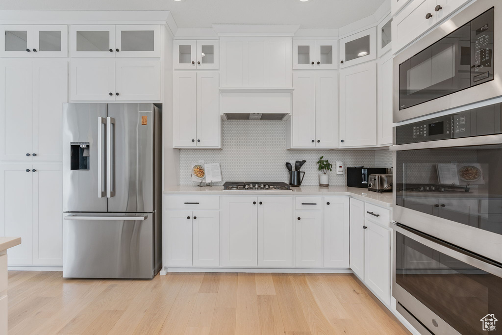 Kitchen featuring white cabinets, tasteful backsplash, light wood-type flooring, and stainless steel appliances