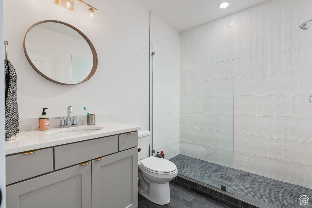 Bathroom featuring tile floors, vanity with extensive cabinet space, toilet, and tiled shower