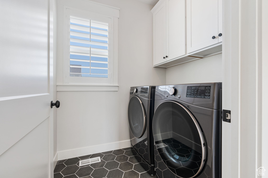 Washroom featuring washer and dryer, dark tile floors, and cabinets