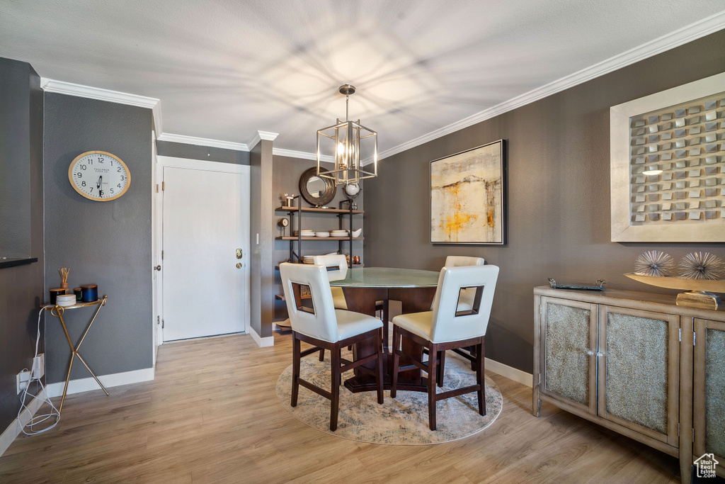 Dining area with light hardwood / wood-style flooring, crown molding, and an inviting chandelier