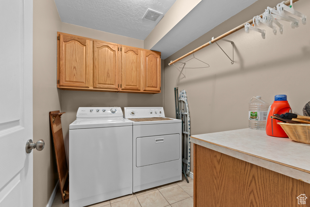 Laundry area featuring a textured ceiling, cabinets, light tile floors, and washer and clothes dryer