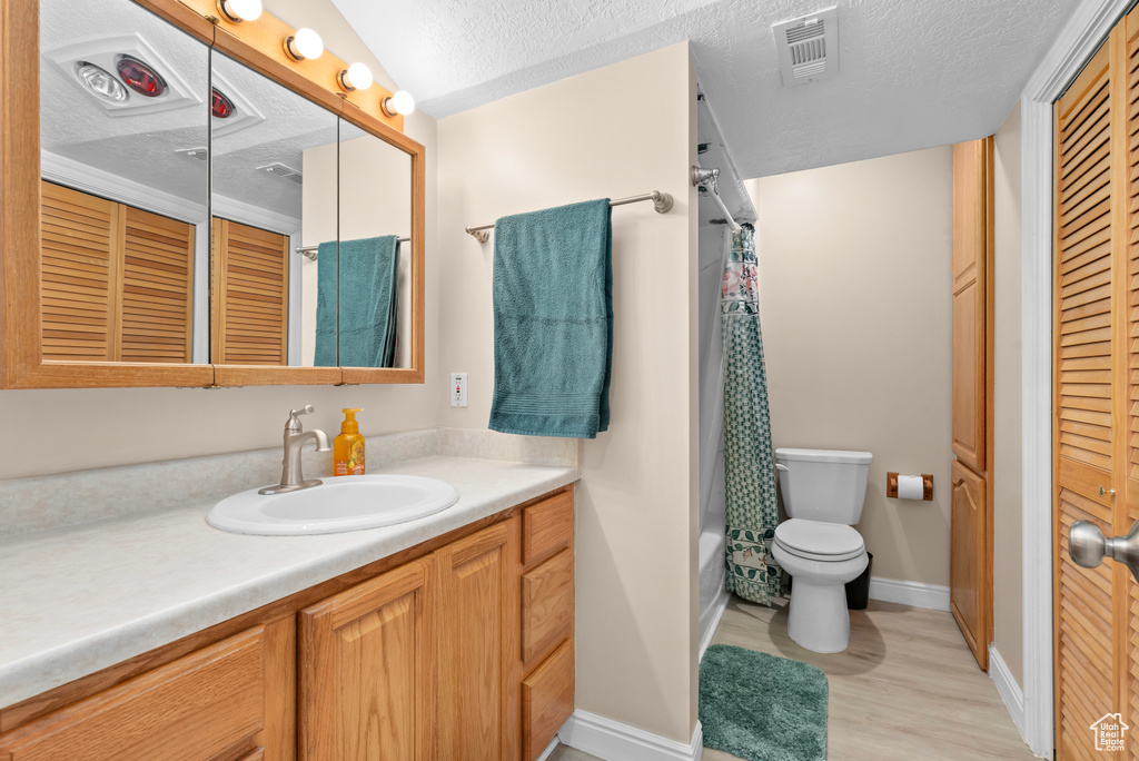 Full bathroom with a textured ceiling, toilet, vanity, hardwood / wood-style flooring, and shower / bathtub combination with curtain