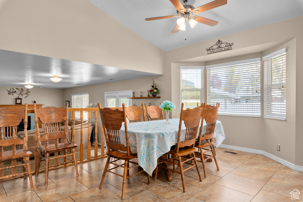 Dining space with ceiling fan, vaulted ceiling, plenty of natural light, and light tile floors