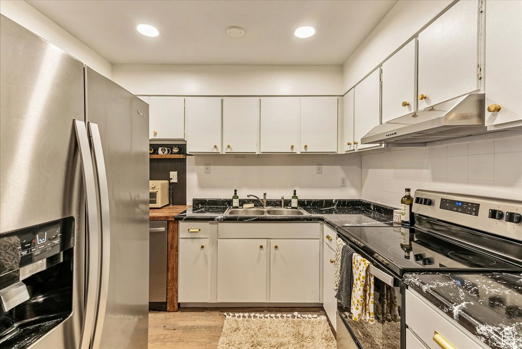 Kitchen with appliances with stainless steel finishes, light hardwood / wood-style floors, white cabinets, and sink