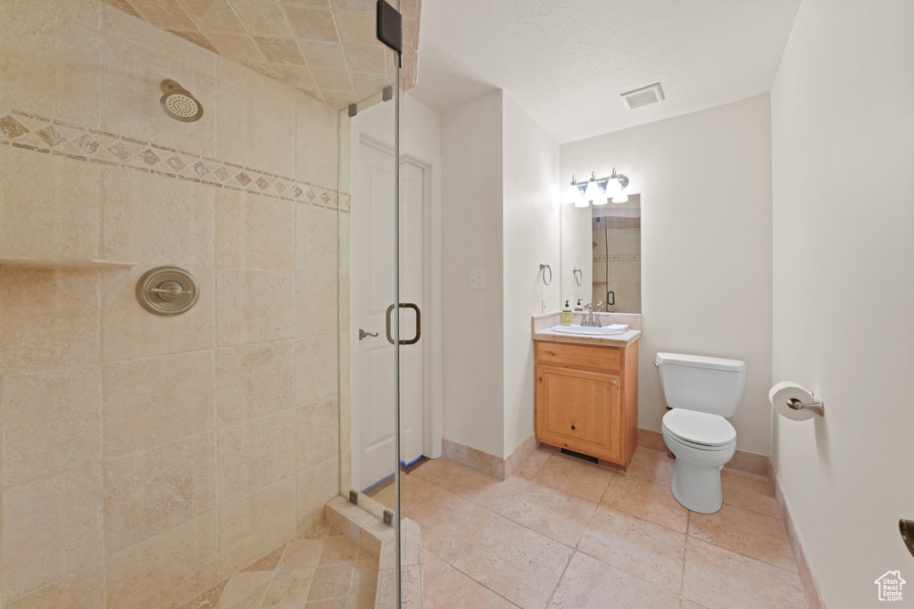 Bathroom featuring tile flooring, oversized vanity, toilet, and a shower with shower door