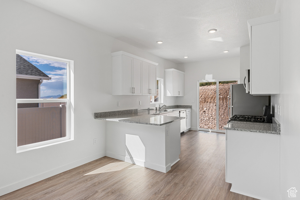 Kitchen with white cabinets, light hardwood / wood-style floors, kitchen peninsula, and light stone countertops