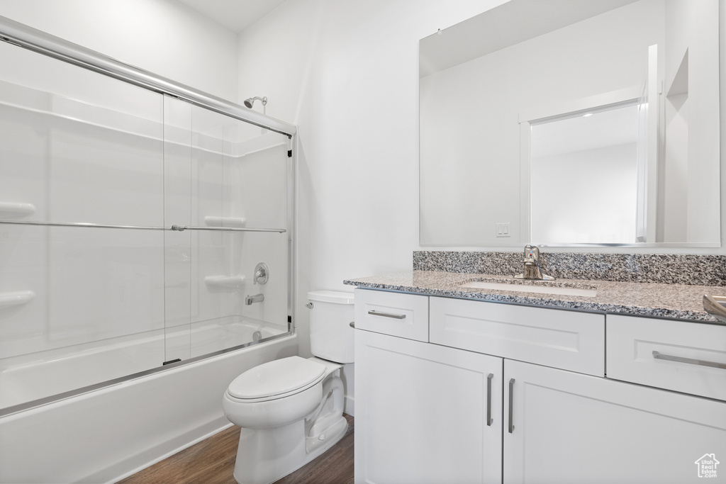 Full bathroom with wood-type flooring, combined bath / shower with glass door, vanity, and toilet