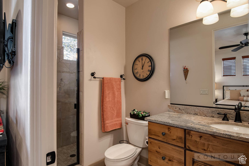 Bathroom featuring a shower with shower door, large vanity, ceiling fan, and toilet