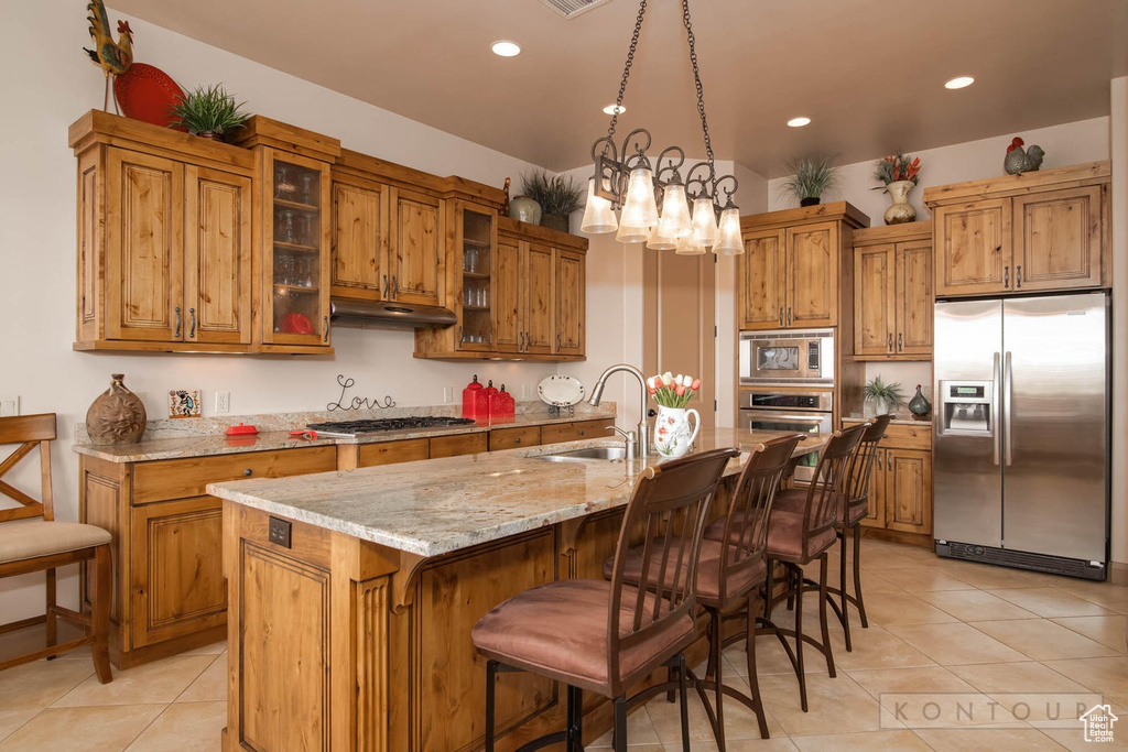 Kitchen with decorative light fixtures, stainless steel appliances, an island with sink, sink, and light tile floors