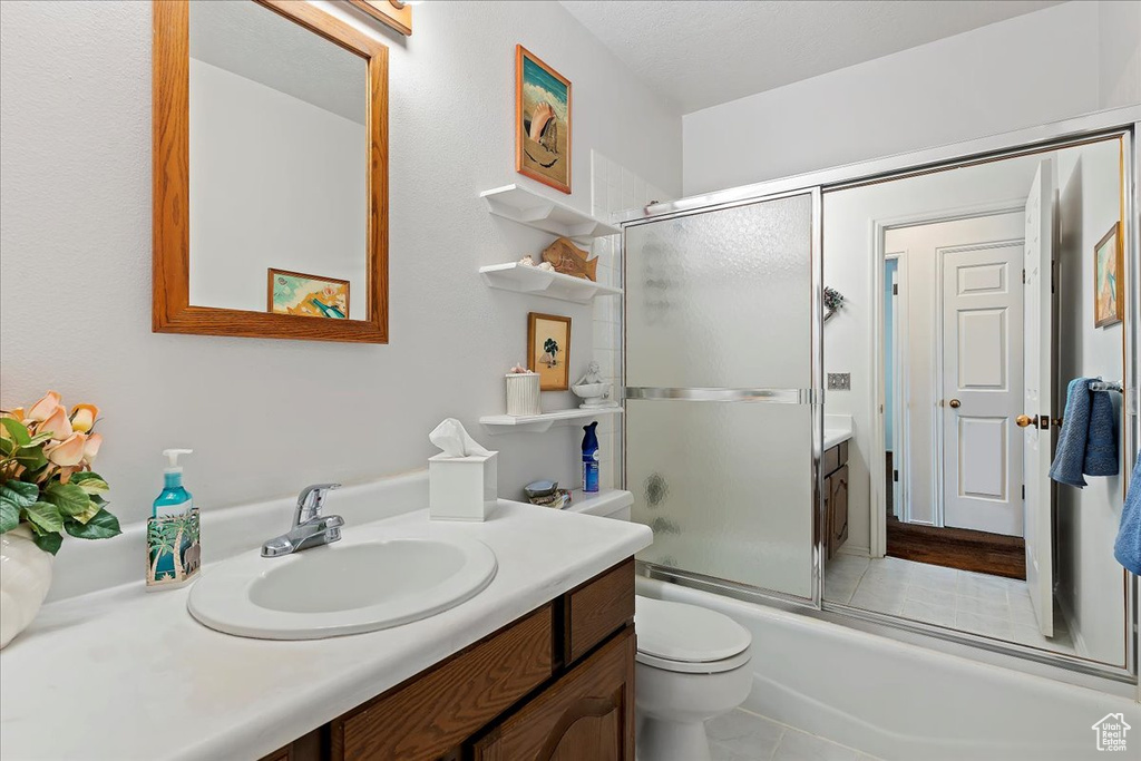 Full bathroom with large vanity, tile floors, toilet, and enclosed tub / shower combo