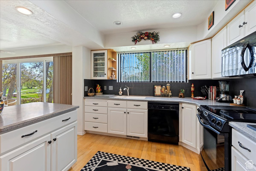 Kitchen featuring white cabinets, black appliances, sink, tasteful backsplash, and light hardwood / wood-style floors