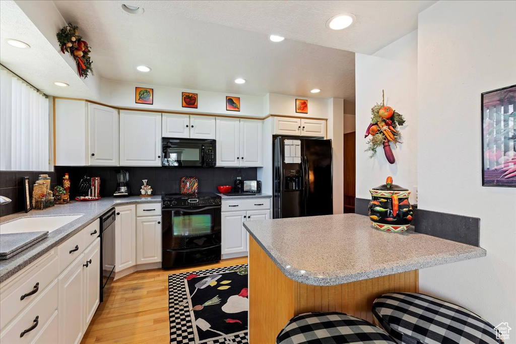 Kitchen featuring white cabinets, tasteful backsplash, light hardwood / wood-style floors, and black appliances