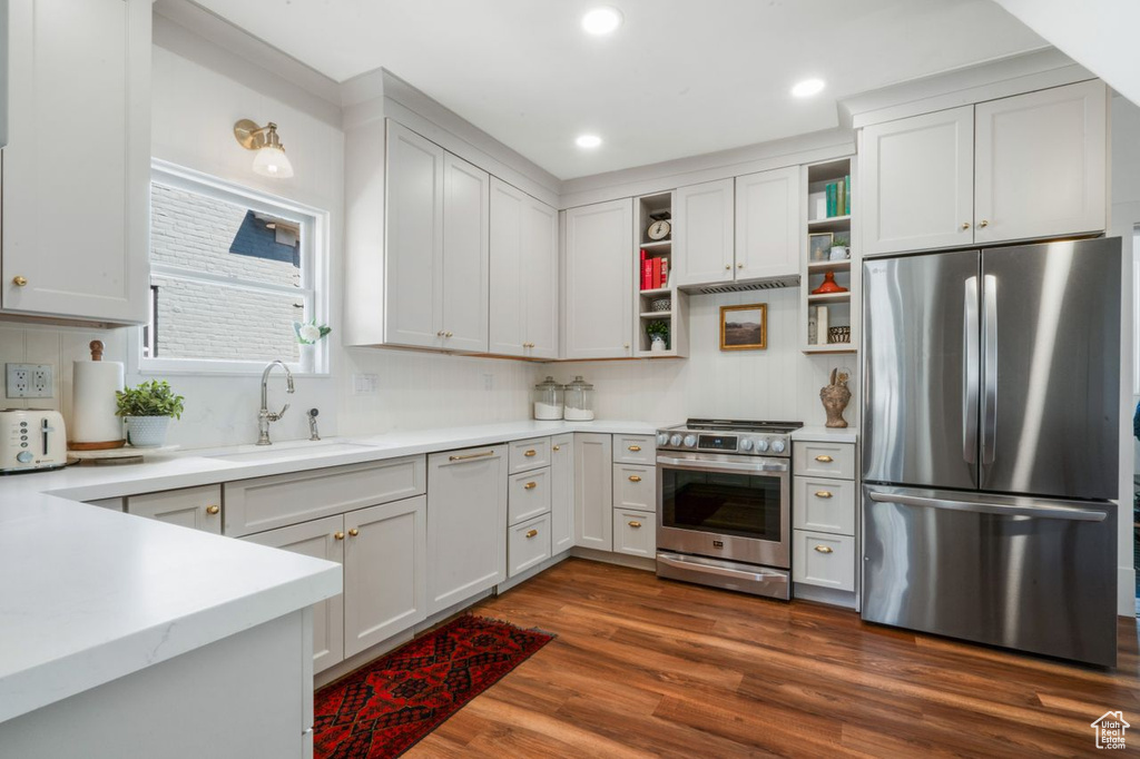 Kitchen with appliances with stainless steel finishes, backsplash, dark hardwood / wood-style floors, white cabinets, and sink