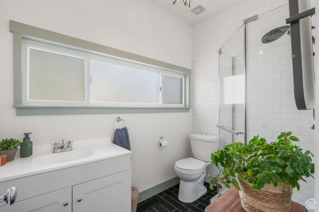 Bathroom featuring a shower with door, vanity with extensive cabinet space, toilet, and tile flooring