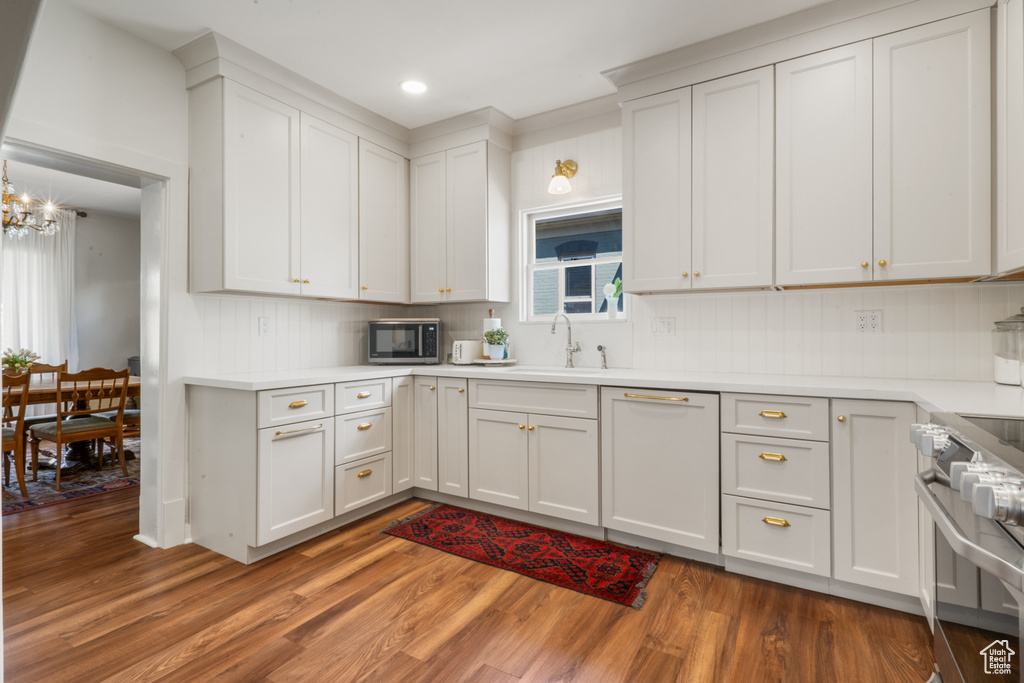 Kitchen with backsplash, stainless steel appliances, hardwood / wood-style flooring, white cabinets, and sink