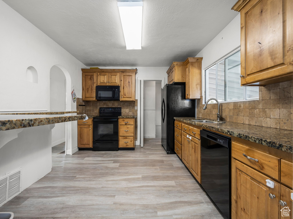 Kitchen with backsplash, black appliances, dark stone countertops, sink, and light wood-type flooring