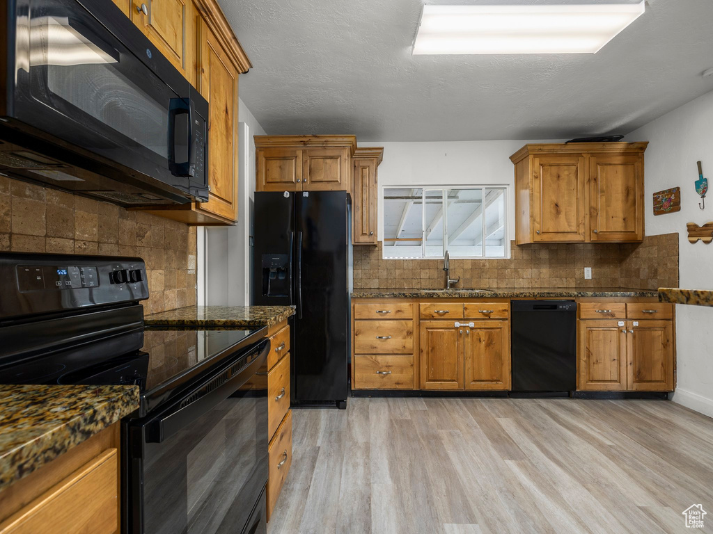 Kitchen featuring backsplash, light hardwood / wood-style floors, black appliances, dark stone counters, and sink