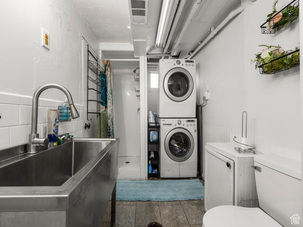 Clothes washing area featuring sink, stacked washing maching and dryer, and tile flooring