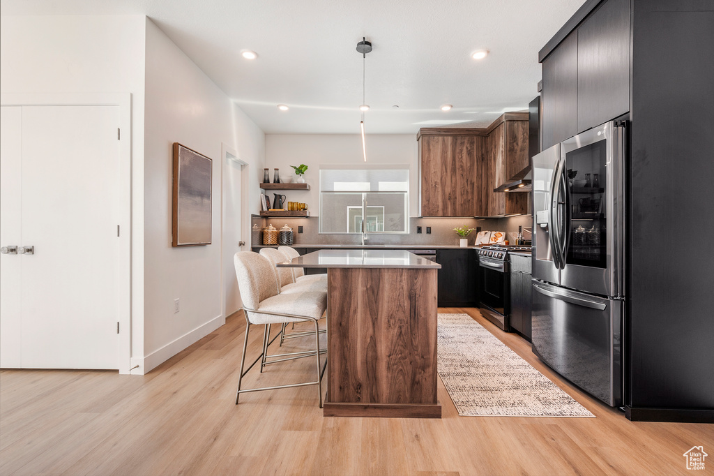 Kitchen with light hardwood / wood-style flooring, a breakfast bar area, stainless steel appliances, and a center island