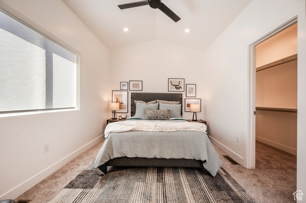 Carpeted bedroom with vaulted ceiling, ceiling fan, a walk in closet, and a closet