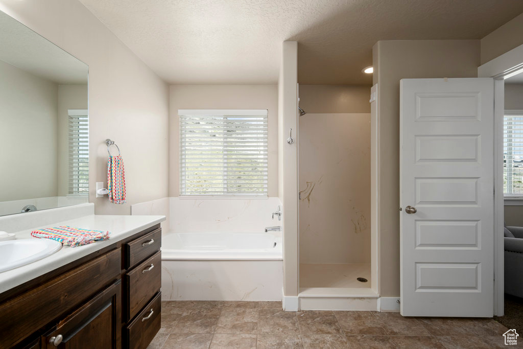 Bathroom featuring plus walk in shower, a wealth of natural light, vanity, and tile floors
