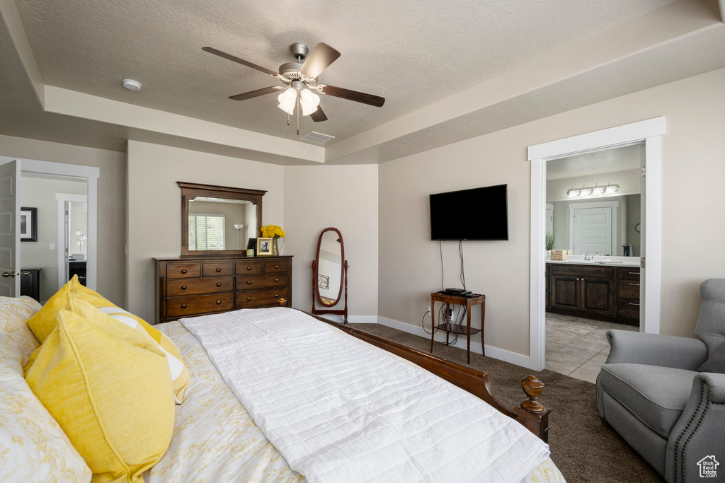 Bedroom featuring ceiling fan, a textured ceiling, ensuite bath, a tray ceiling, and tile floors