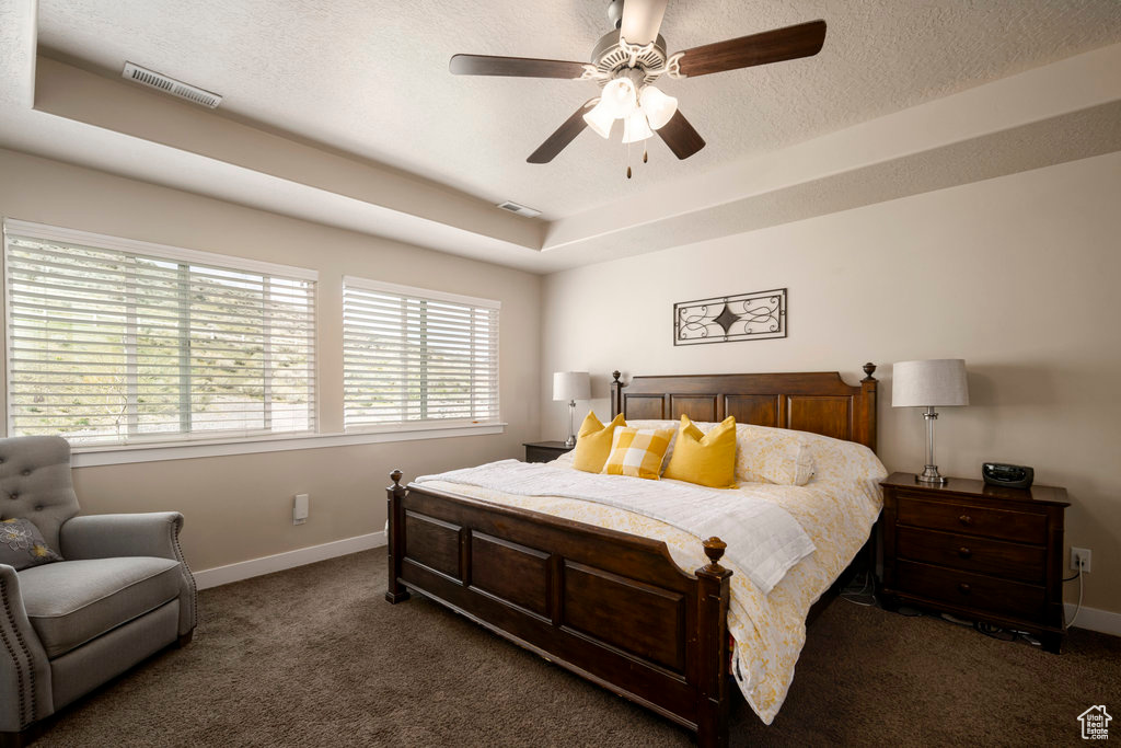 Bedroom featuring a textured ceiling, dark colored carpet, ceiling fan, and a tray ceiling
