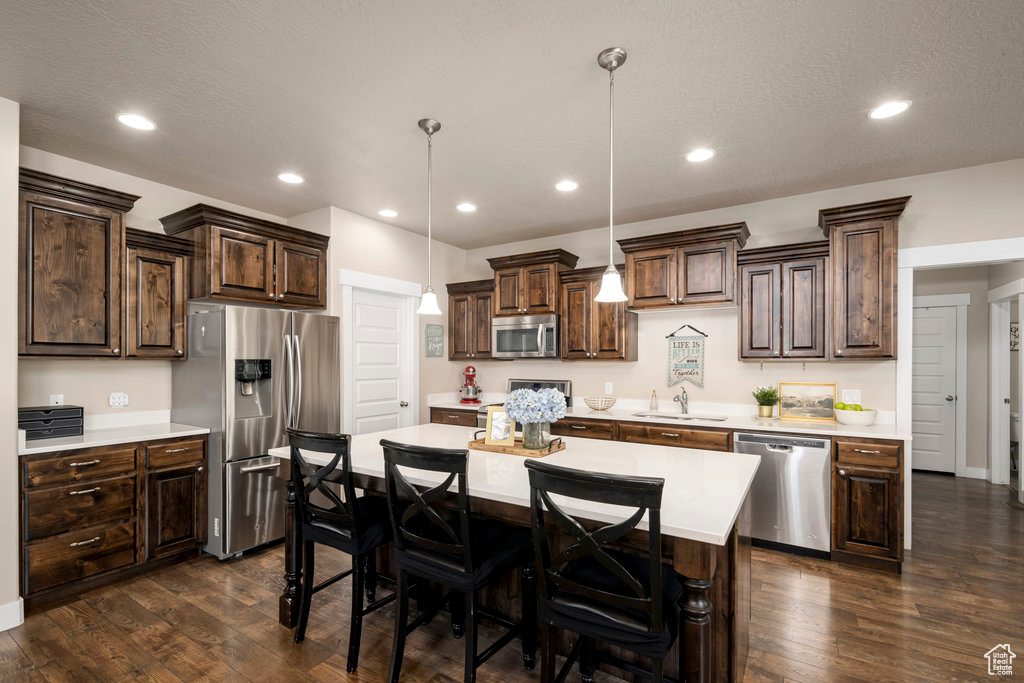 Kitchen featuring a center island, sink, dark hardwood / wood-style flooring, hanging light fixtures, and stainless steel appliances