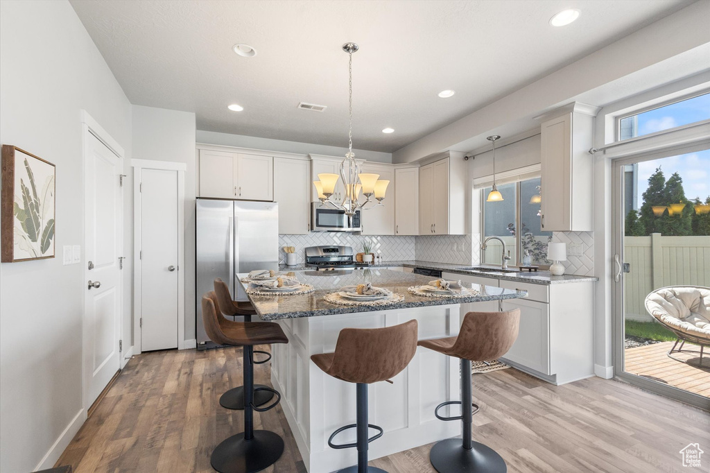 Kitchen with wood-type flooring, decorative light fixtures, stainless steel appliances, tasteful backsplash, and dark stone countertops
