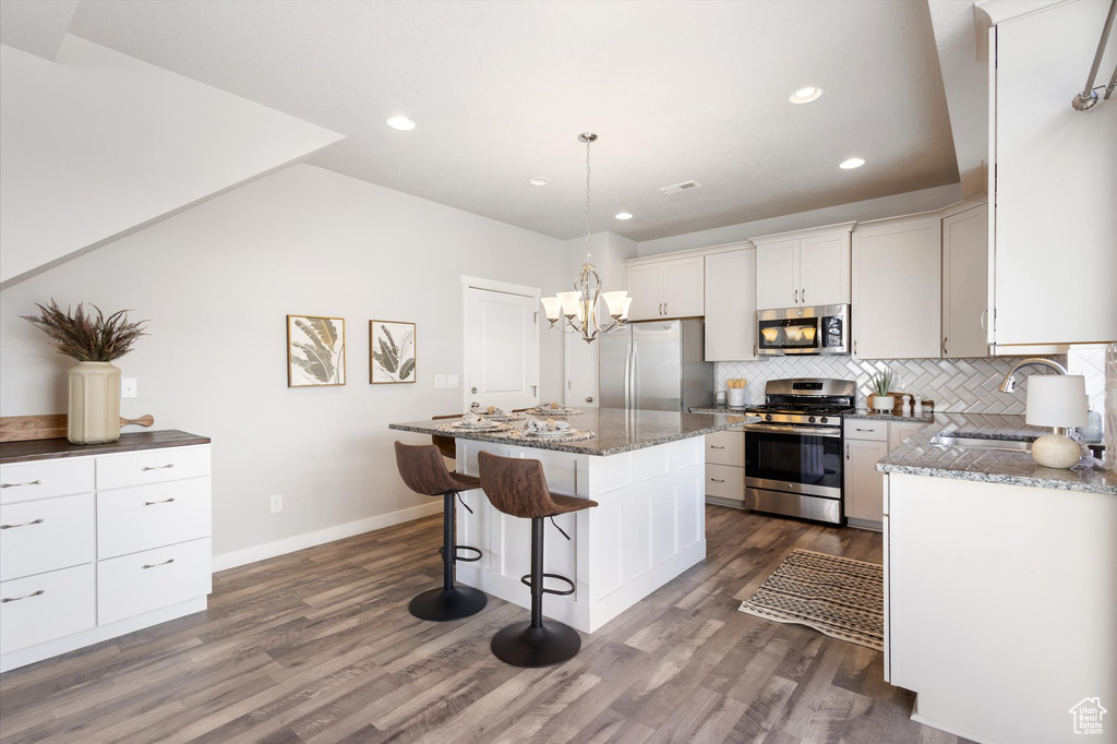 Kitchen with hardwood / wood-style flooring, stainless steel appliances, backsplash, and a kitchen island