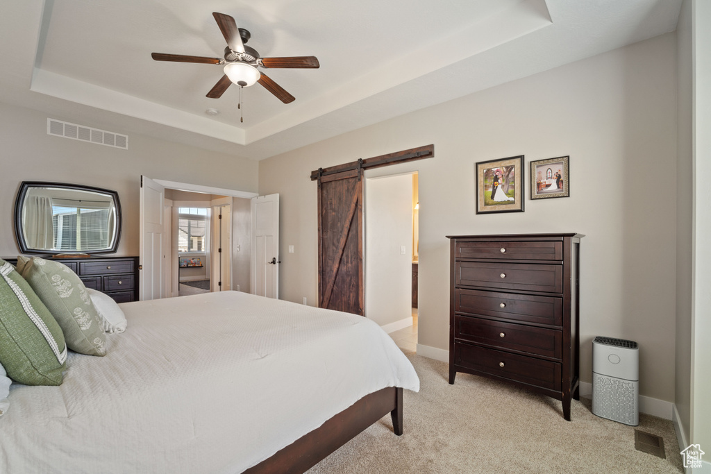 Carpeted bedroom featuring ceiling fan, a barn door, and a tray ceiling