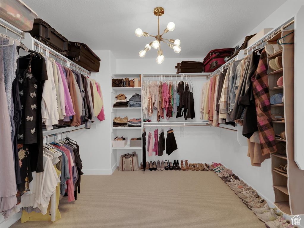 Walk in closet with an inviting chandelier and carpet flooring