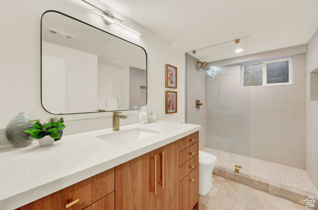 Bathroom with large vanity, tiled shower, toilet, and tile flooring