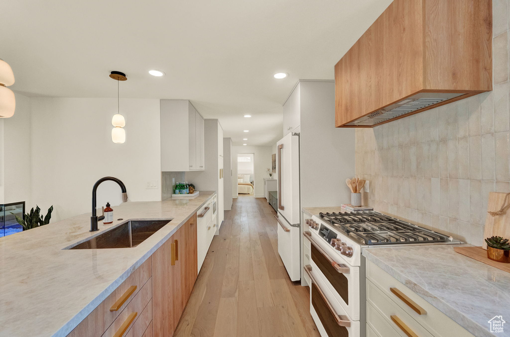 Kitchen with decorative light fixtures, white appliances, light hardwood / wood-style flooring, white cabinetry, and sink